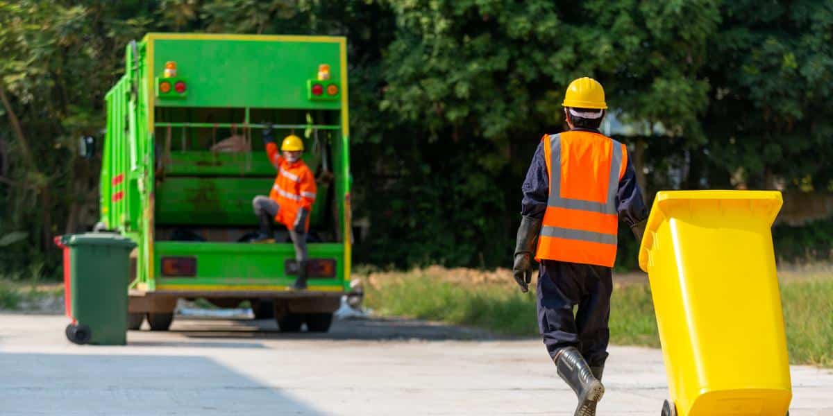 two waste management employees practicing safe workplace practices to reduce risks and injuries.