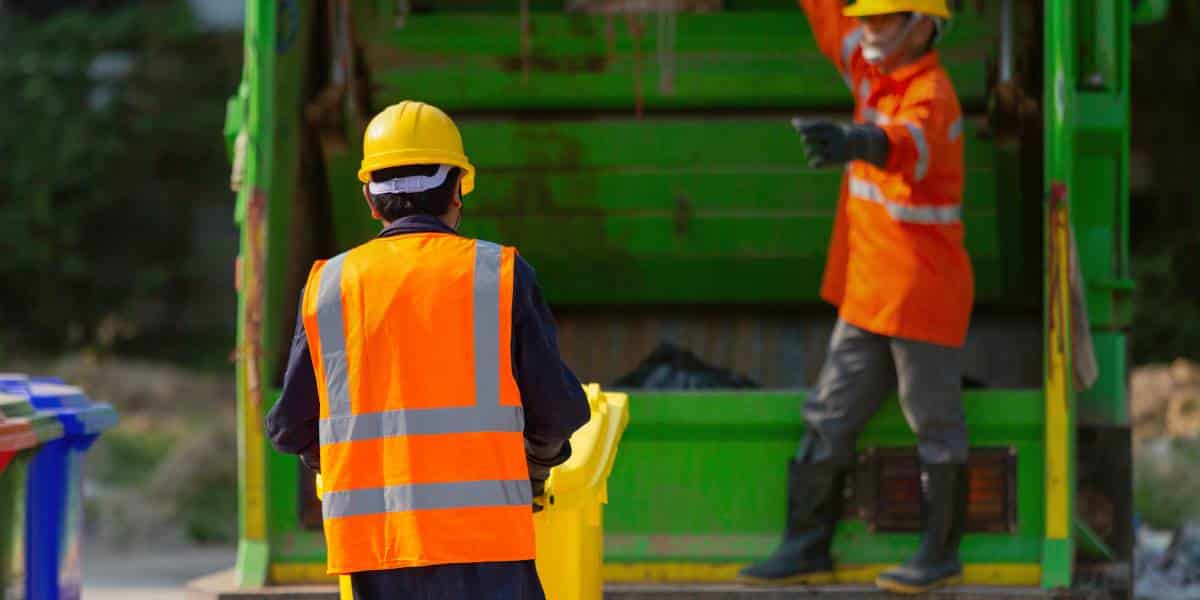 two sanitation workers in orange vests and yellow hard hats who have sanitation employee injury insurance